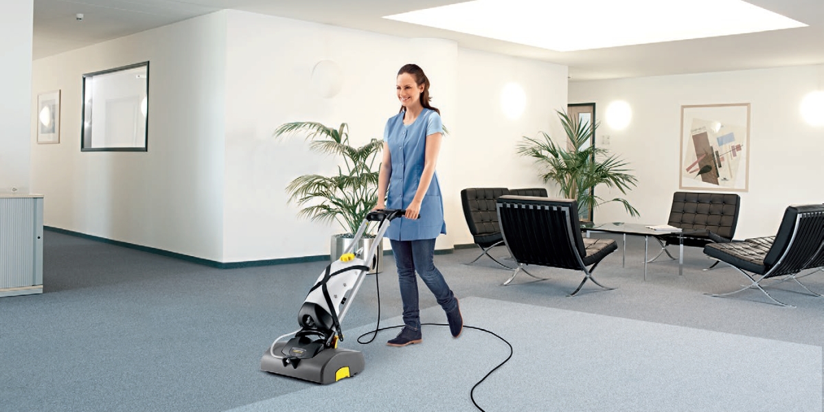 Profesjonalne, kompaktowe urządzenie do czyszczenia wykładzin BRS 43/500 C firmy Karcher. Kobieta czyszcząca wykładzinę podłogową na korytarzu w budynku biurowym przy pomocy BRS 43/500 C firmy Karcher.