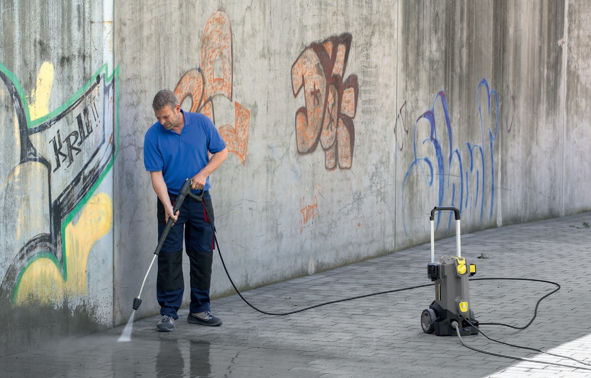 Profesjonalna myjka wysokociśnieniowa HD 5/17 C firmy Karcher podczas mycia chodnika i ścian z graffiti.